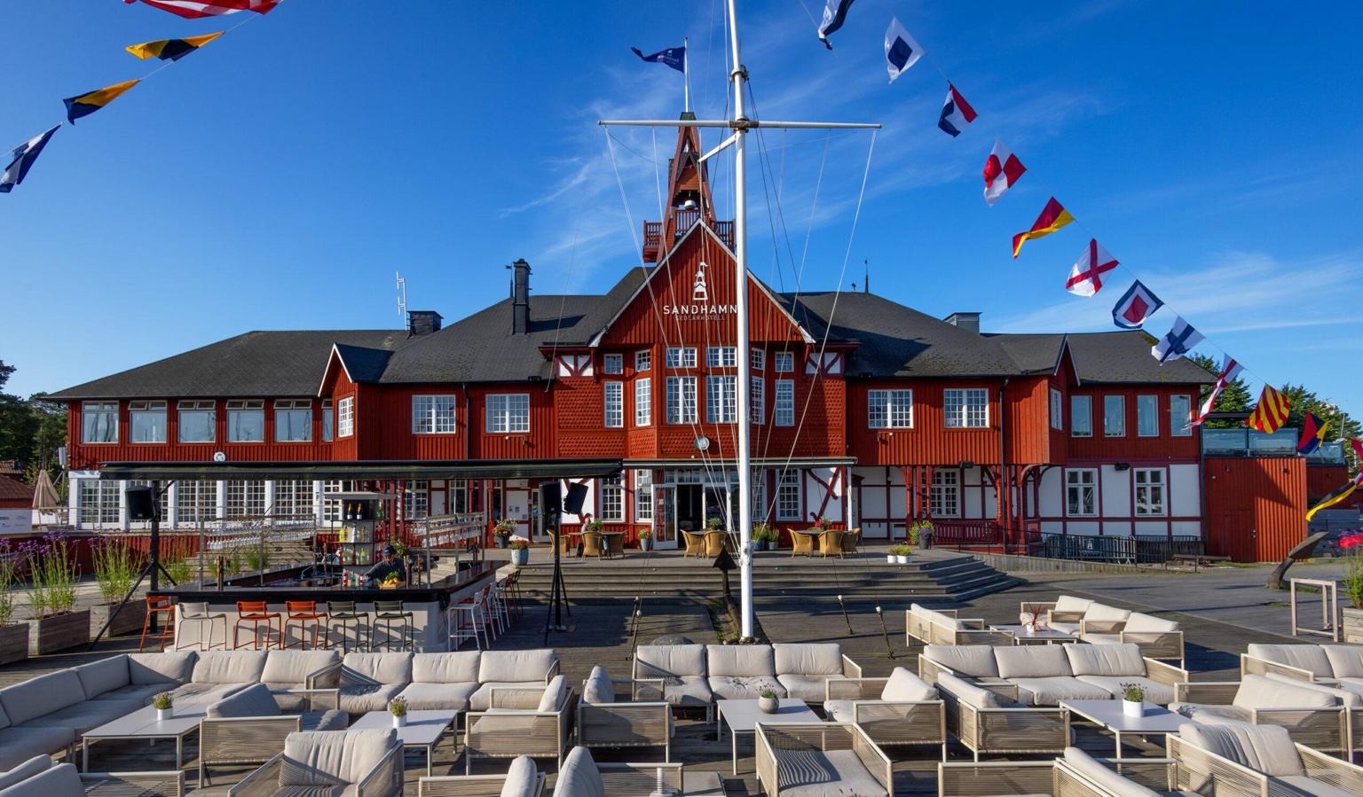 Sandhamn Seglarhotell's red wooden facade with an outdoor deck, lounge seating and nautical signal flags